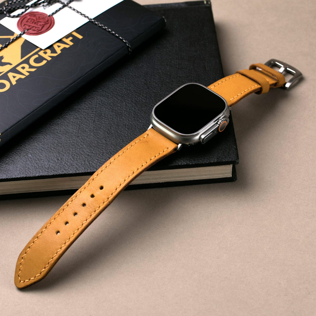 Roarstraps el yapımı deri Apple Watch kayışı, şık tasarımıyla kitap üzerinde sergileniyor.